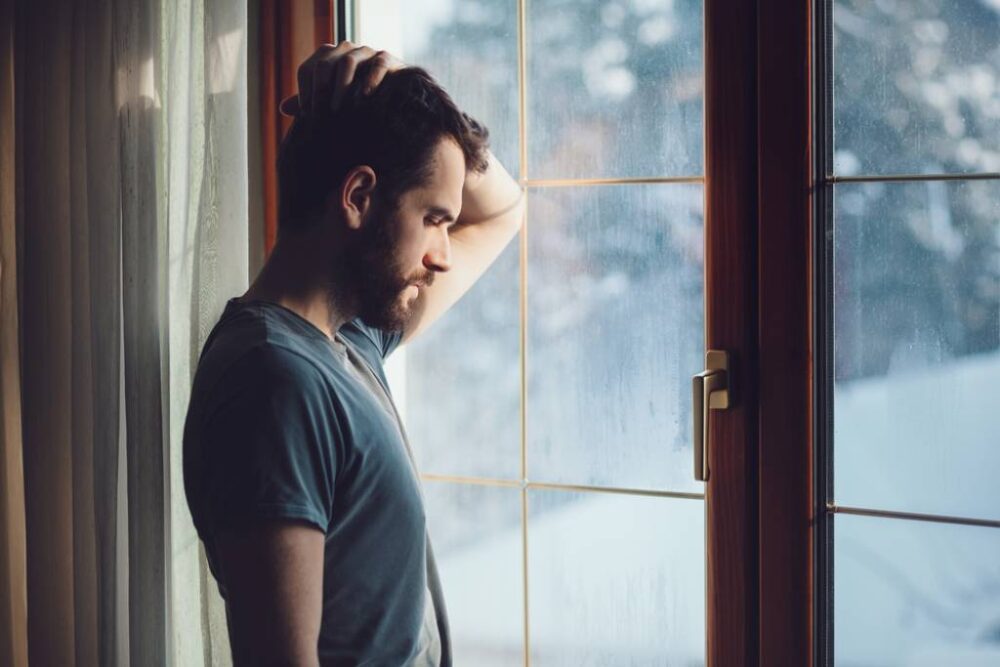 A sad man looking out of the window on a rainy day.