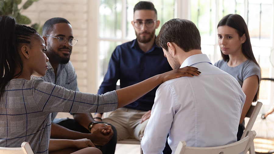 A woman comforts a man during a group therapy session.