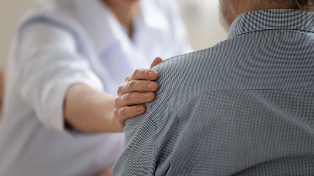 A person consoling another with their hand on their shoulder.