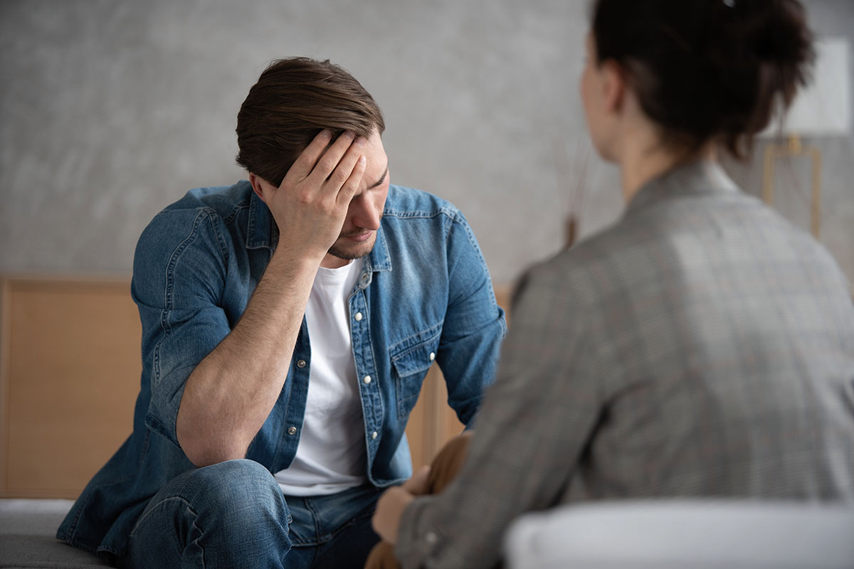 A psychologist talking to a patient with his head in his hand.