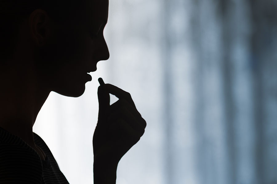 A person in silhouette takes a pill.