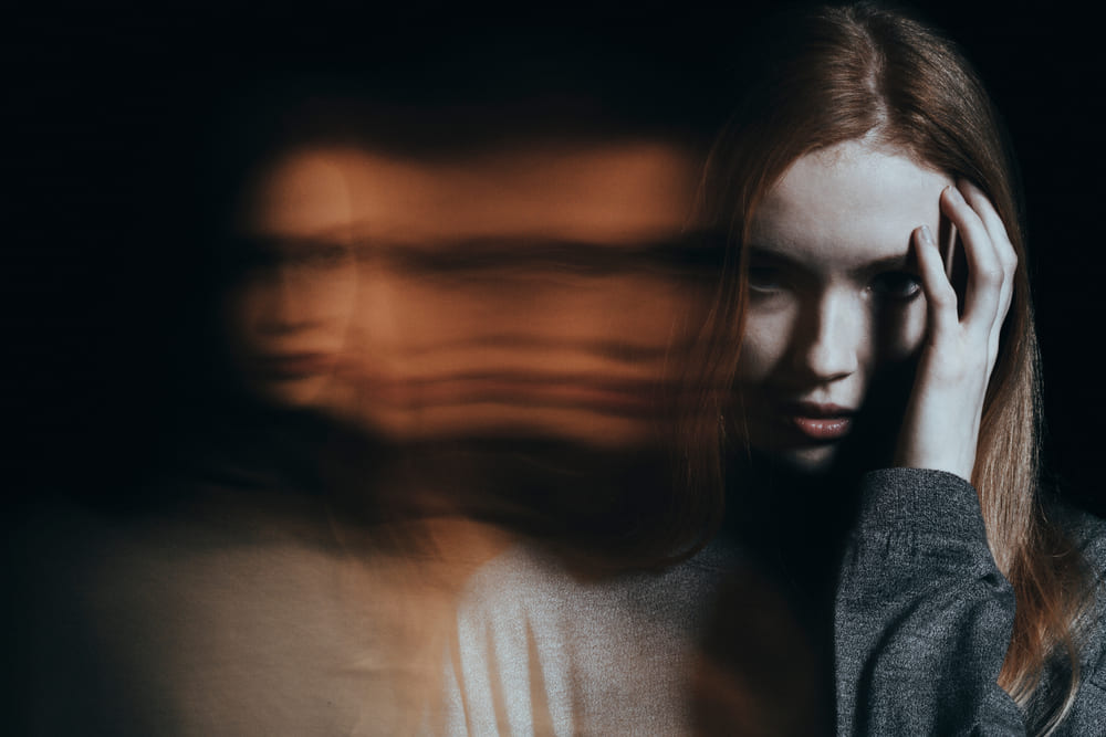 A girl touching her head next to a blurry version of herself.