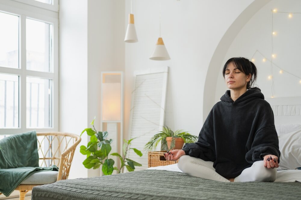 A woman in a yoga pose while meditating on her bed 