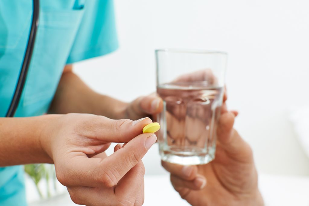 A nurse handing over a pill with a glass of water