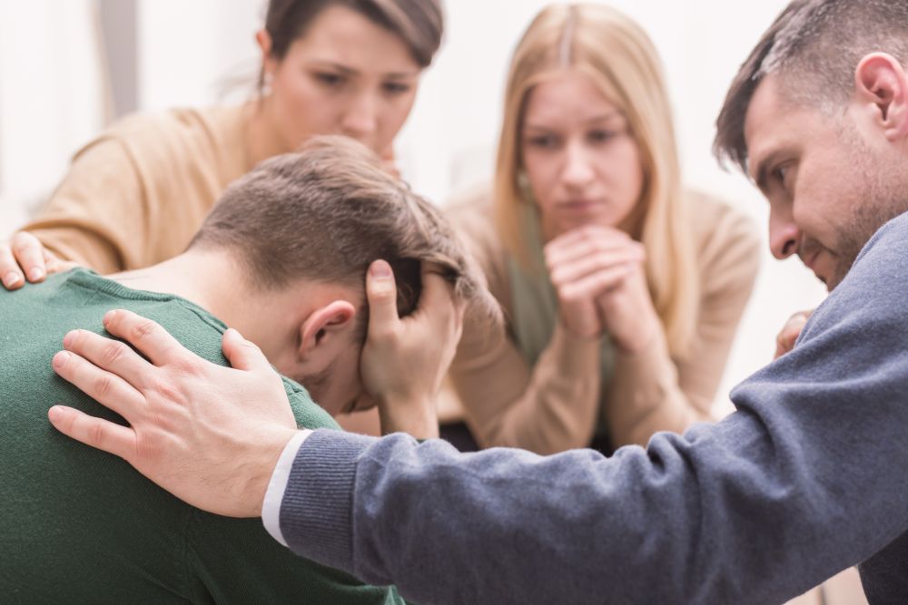 A sad young man being comforted by family